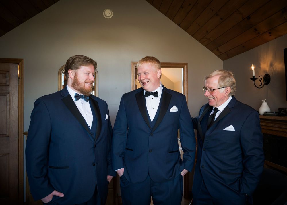 A group of groomsmen in navy blue suits share a candid moment while getting ready for a wedding ceremony.