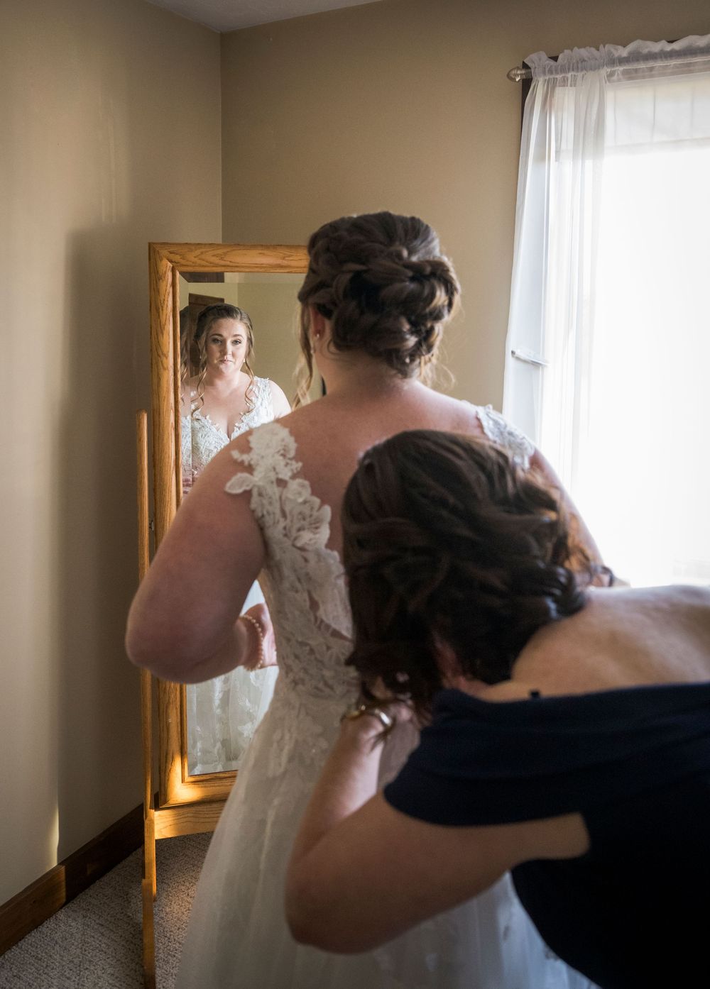 Wedding dress being fitted and adjusted in a sunlit dressing room.