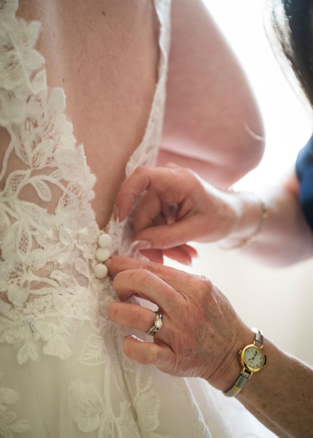Close-up of hands fastening delicate buttons on a white lace wedding dress.
