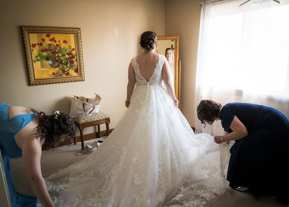 Wedding dress preparation scene in a sunlit room with vintage furniture.