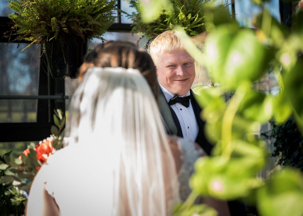 An outdoor wedding ceremony moment captured through greenery and natural sunlight.
