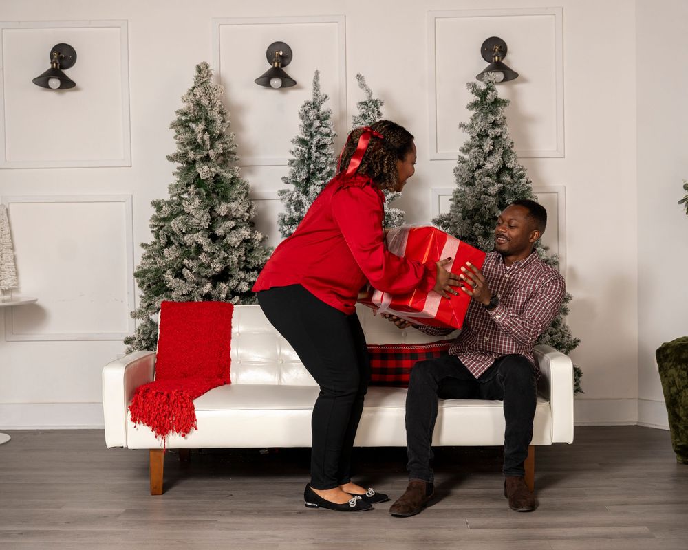 A couple wearing red and gray outfits dances together in front of a decorated Christmas tree during a studio photoshoot.