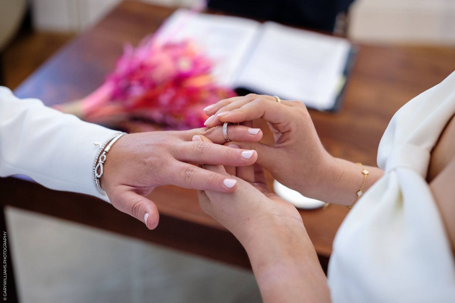 Close up of hands exchanging wedding rings during a ceremony at a wooden table.
