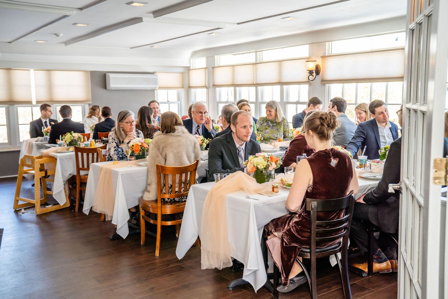 A panoramic view of an elegant restaurant dining room with white tablecloths and large windows letting in natural light.