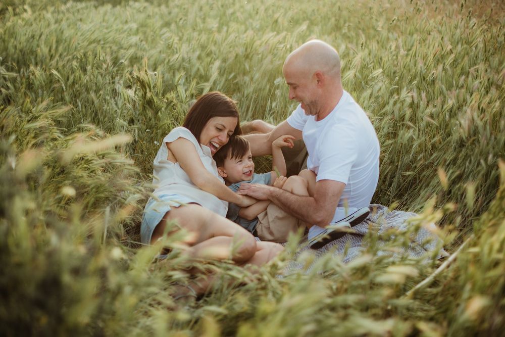 Happy family of four sitting together in a lush green field on a sunny day.