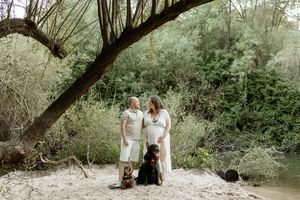 Family portrait with two dogs under a curved tree branch by a river.