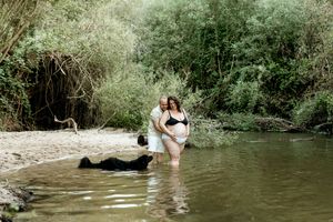 Couple wading in river water during outdoor photoshoot.