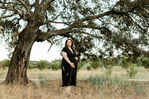 Maternity portrait under large oak tree in rustic field setting.