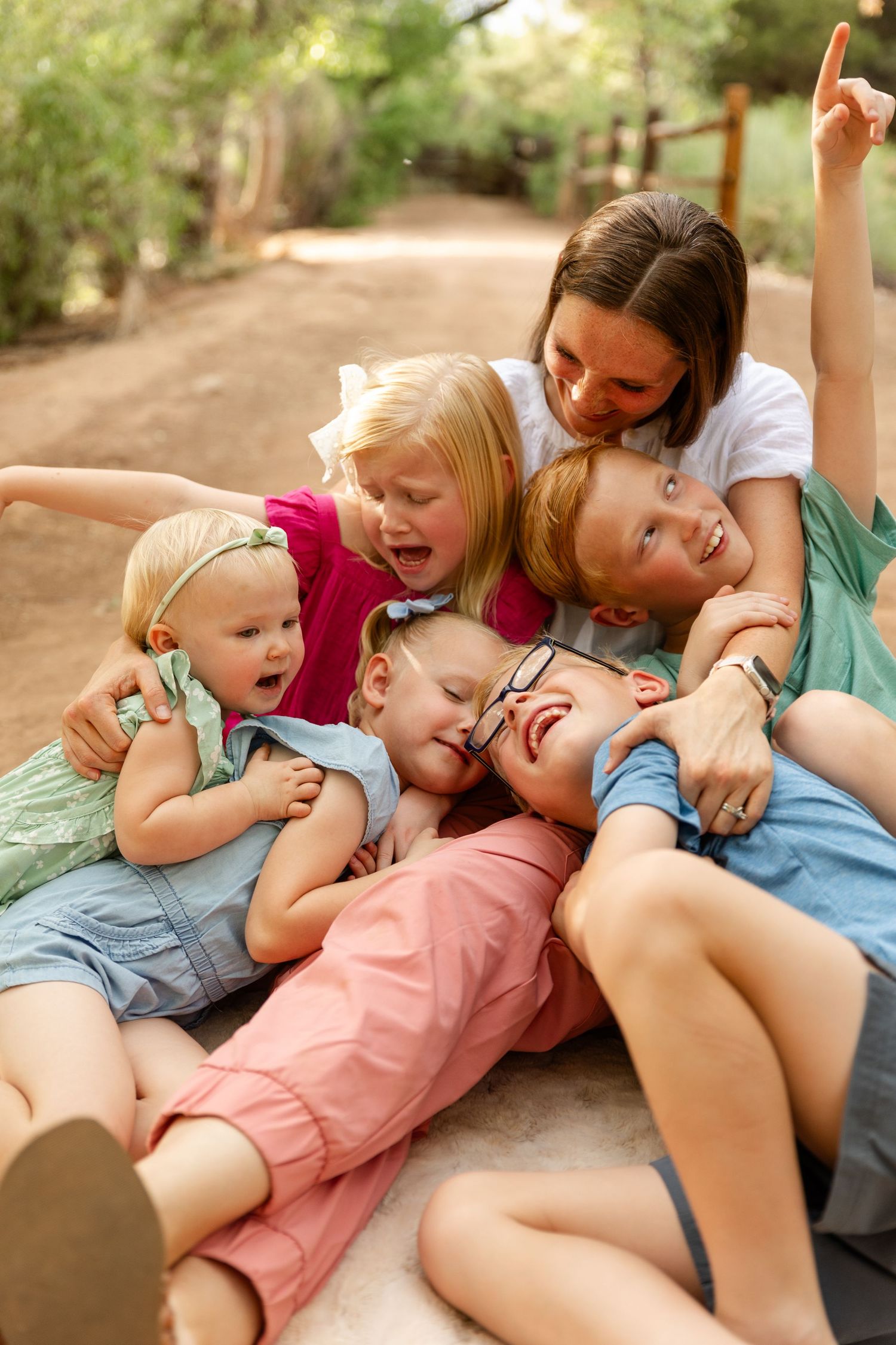 a mother lovingly holding her 5 children playfully on the ground in a pile with all smiles