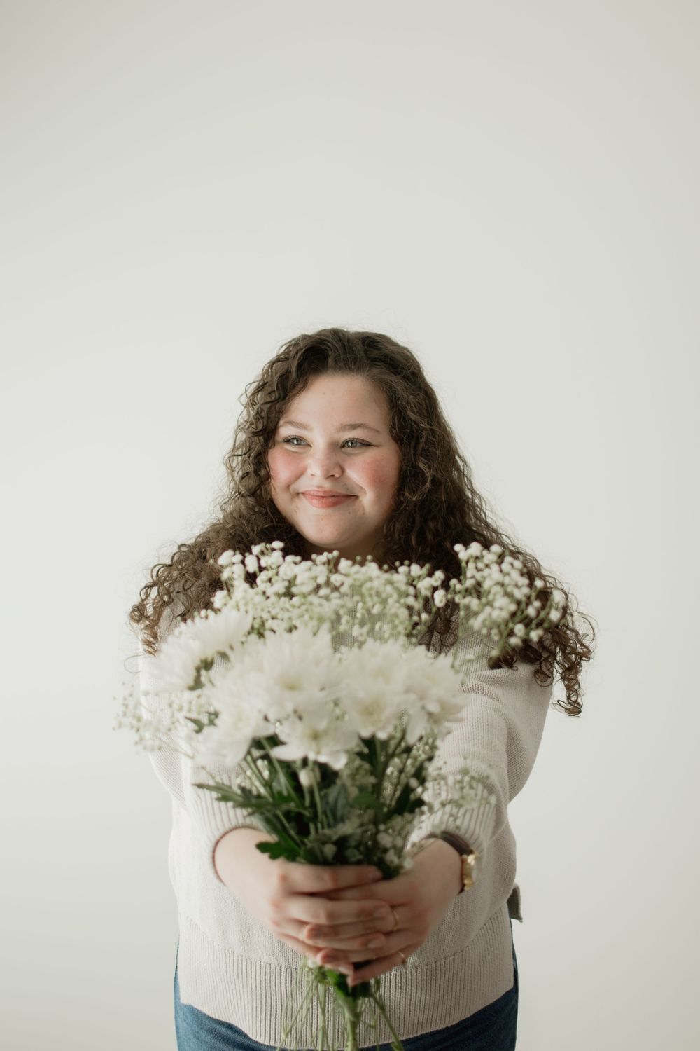 Person in white sweater holds a beautiful bouquet of fresh white baby's breath flowers against a light background.