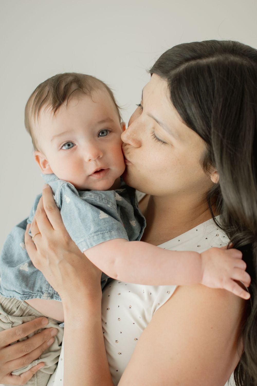 A tender moment between a mother and baby in matching light blue outfits as they share loving cuddles and kisses.