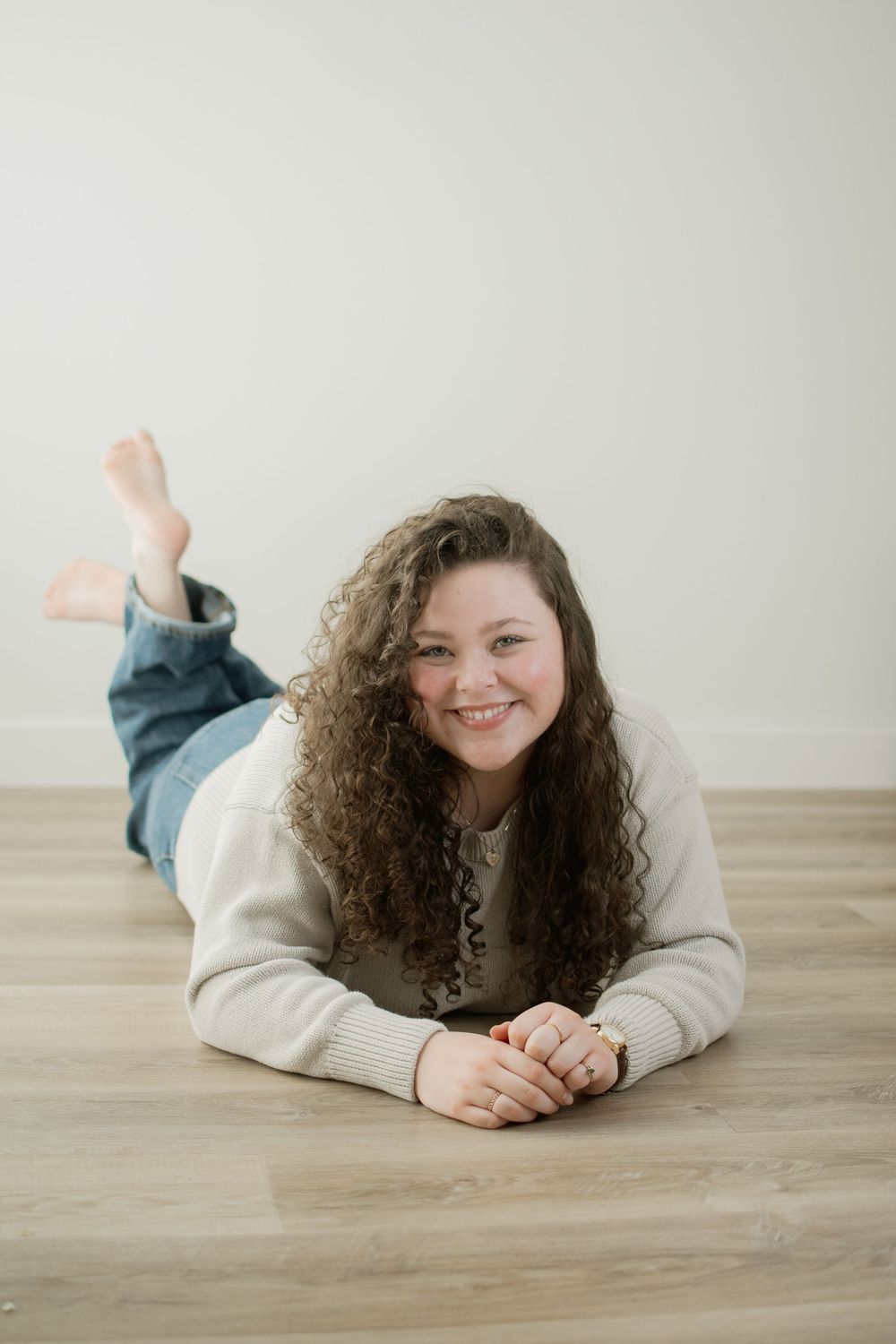 Person with curly dark hair wearing a cream sweater lies casually on wooden floor in three casual poses.