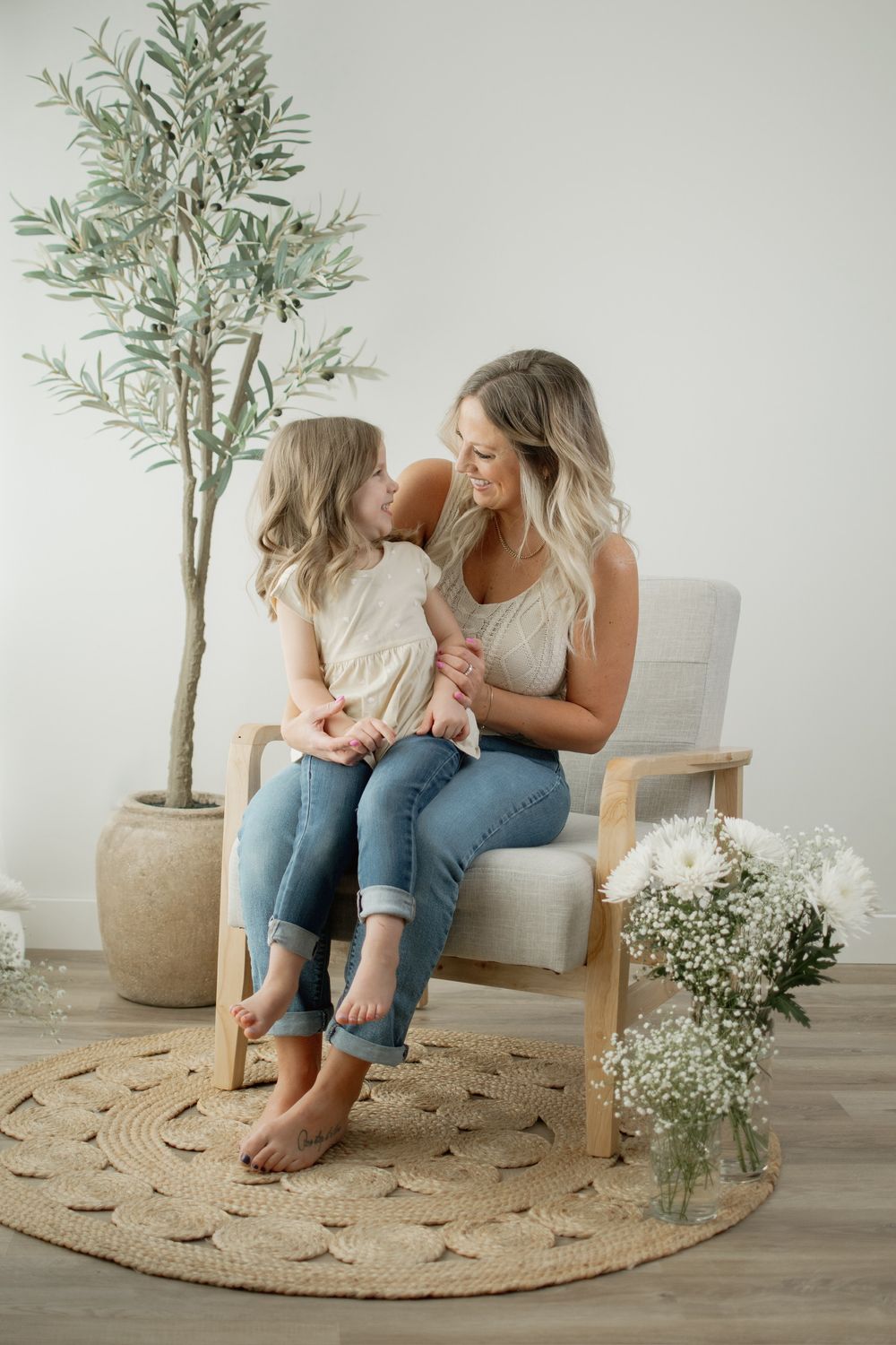 A tender moment shared in a minimalist living space with a round jute rug and potted olive tree in the background.