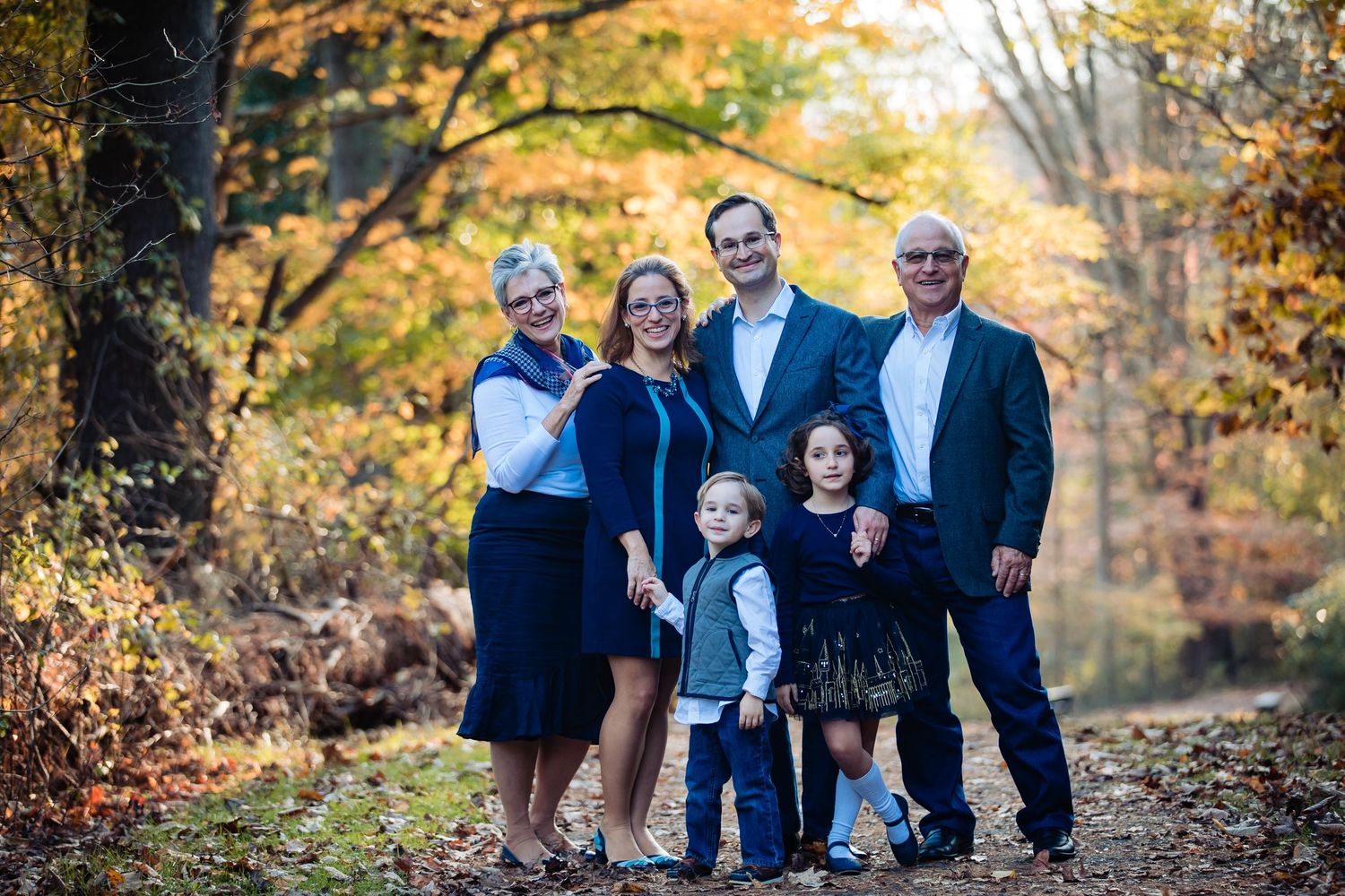 A group wearing coordinated navy blue outfits poses together on a path surrounded by vibrant autumn foliage.