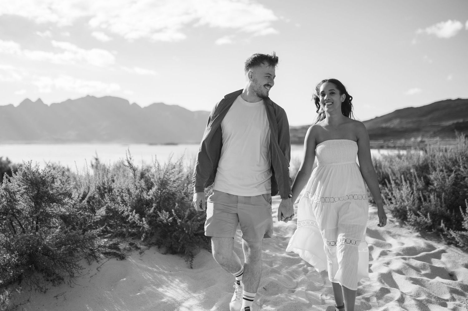 Black and white desert engagement photoshoot with mountains and sagebrush in the background under cloudy skies.