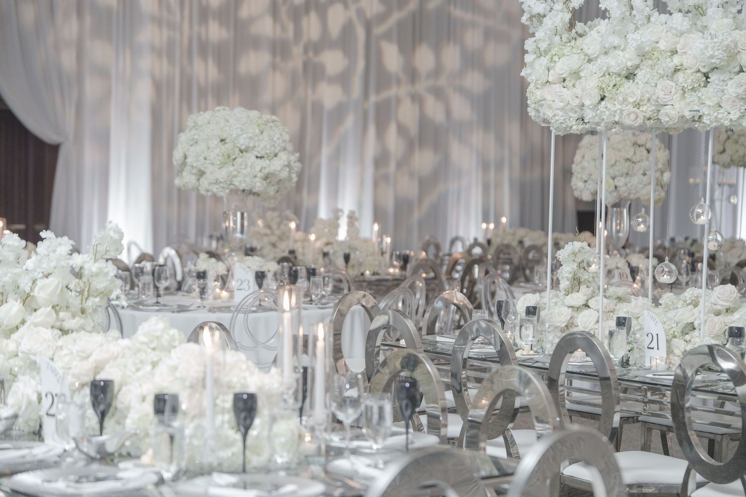 Elegant white wedding reception decor with crystal candelabras and hydrangea centerpieces on mirrored tables.