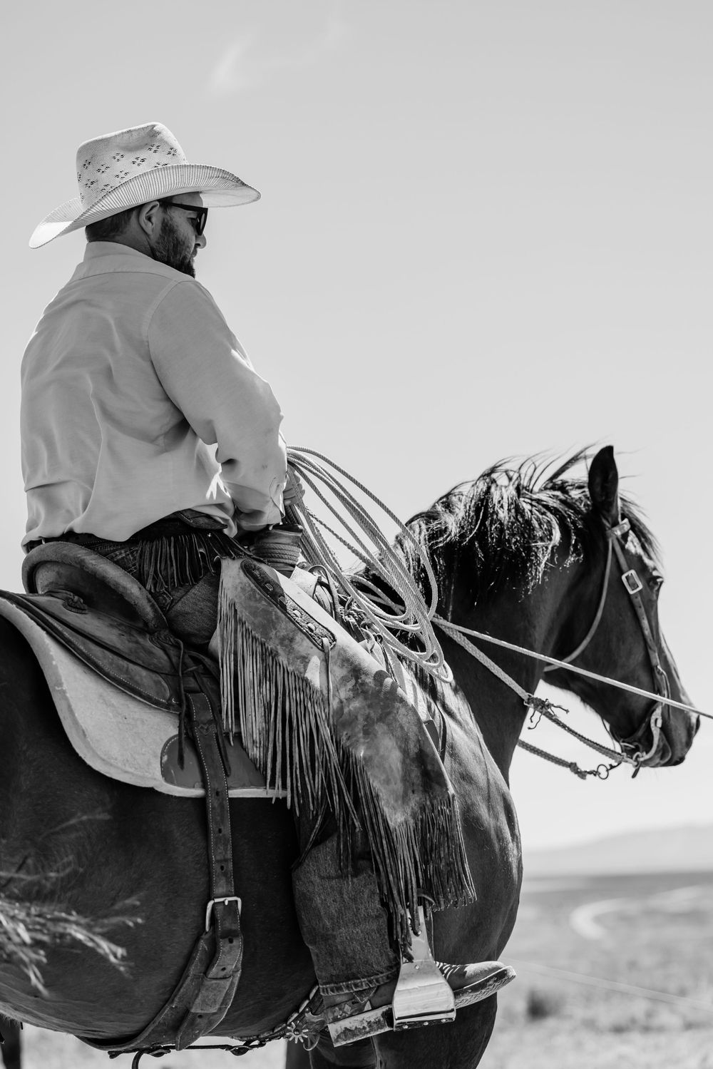 Close-up black and white profile view of cowboys riding horses across rugged western terrain.