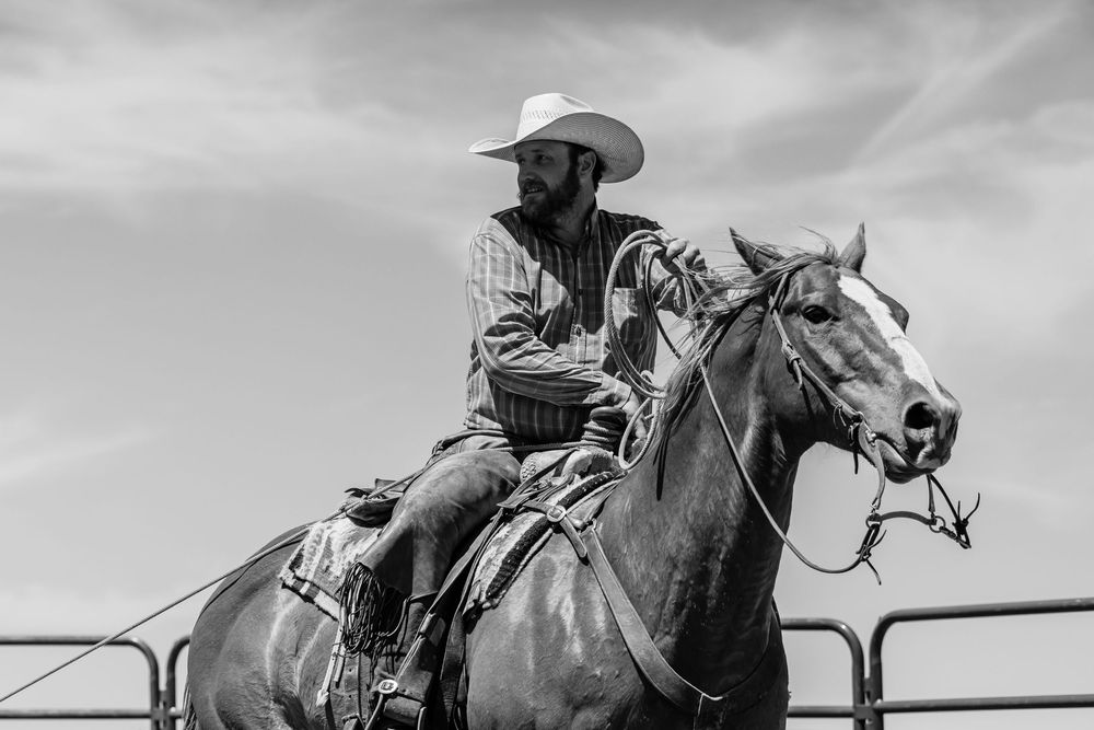 Cowboy on horseback against dramatic sky in western ranch setting.