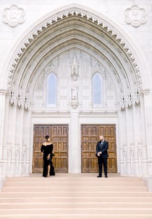 Inside a gothic chapel with ornate arched doorways and cathedral ceilings, two figures stand distant from each other.
