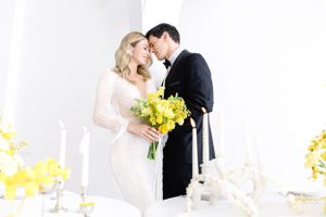 Romantic wedding couple share intimate moment at elegantly decorated reception table with yellow flowers.