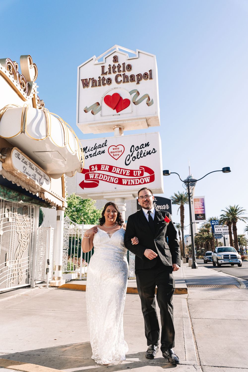 A couple poses in front of the iconic Little White Chapel in Las Vegas under clear blue skies.