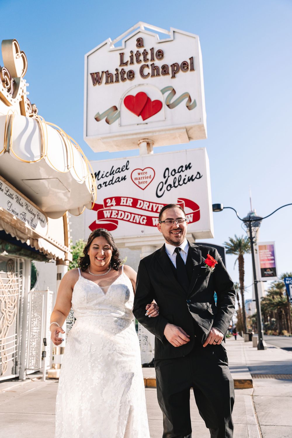 Couple poses playfully in front of Little White Chapel signs in Las Vegas during their wedding day.