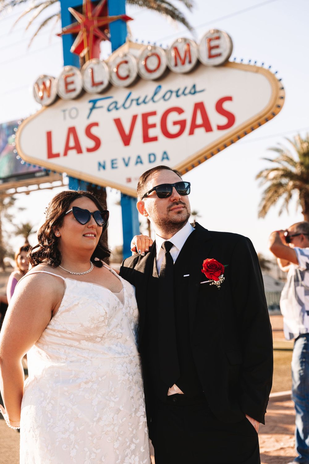 Couple poses together at iconic Welcome to Las Vegas sign with palm trees in background.