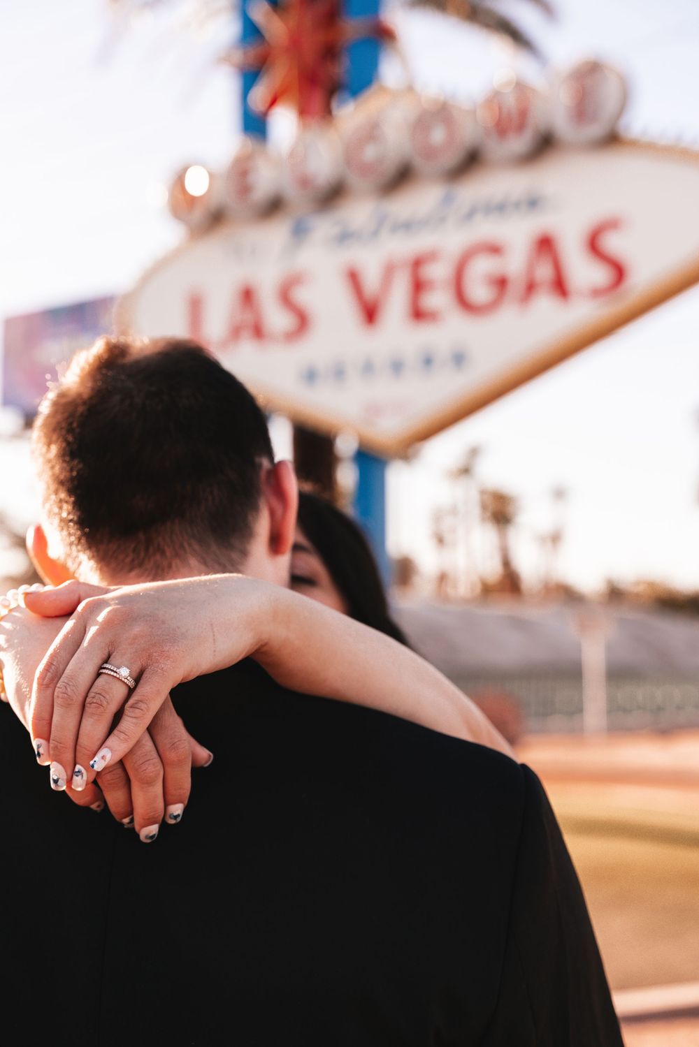 A married couple holds hands in front of the iconic Las Vegas welcome sign at dusk.