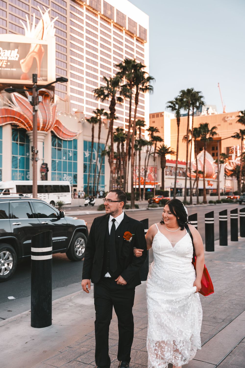 Couple celebrates their wedding on Las Vegas Strip with palm trees and casino buildings in warm sunset lighting.