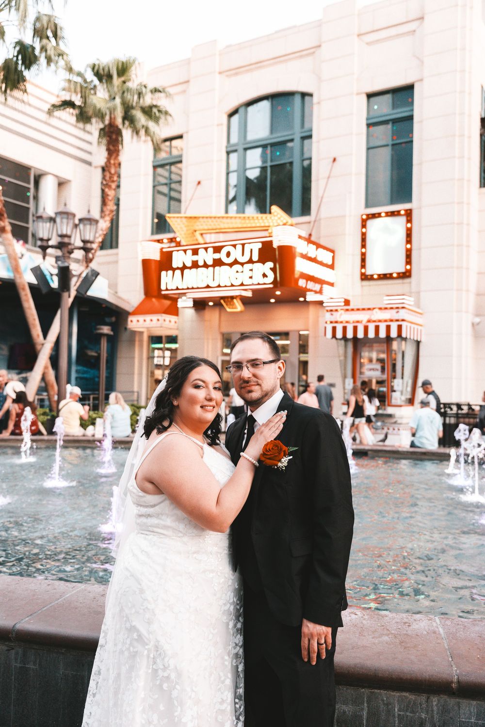 A romantic wedding photoshoot series with a couple posing near a fountain at an In-N-Out restaurant exterior.