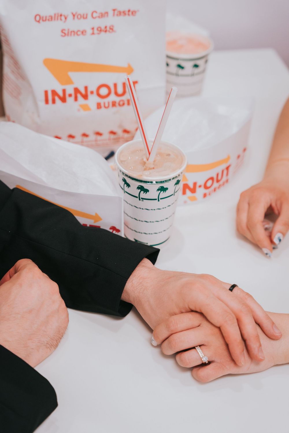 Two hands rest on a white surface next to In-N-Out Burger branded cups and packaging.