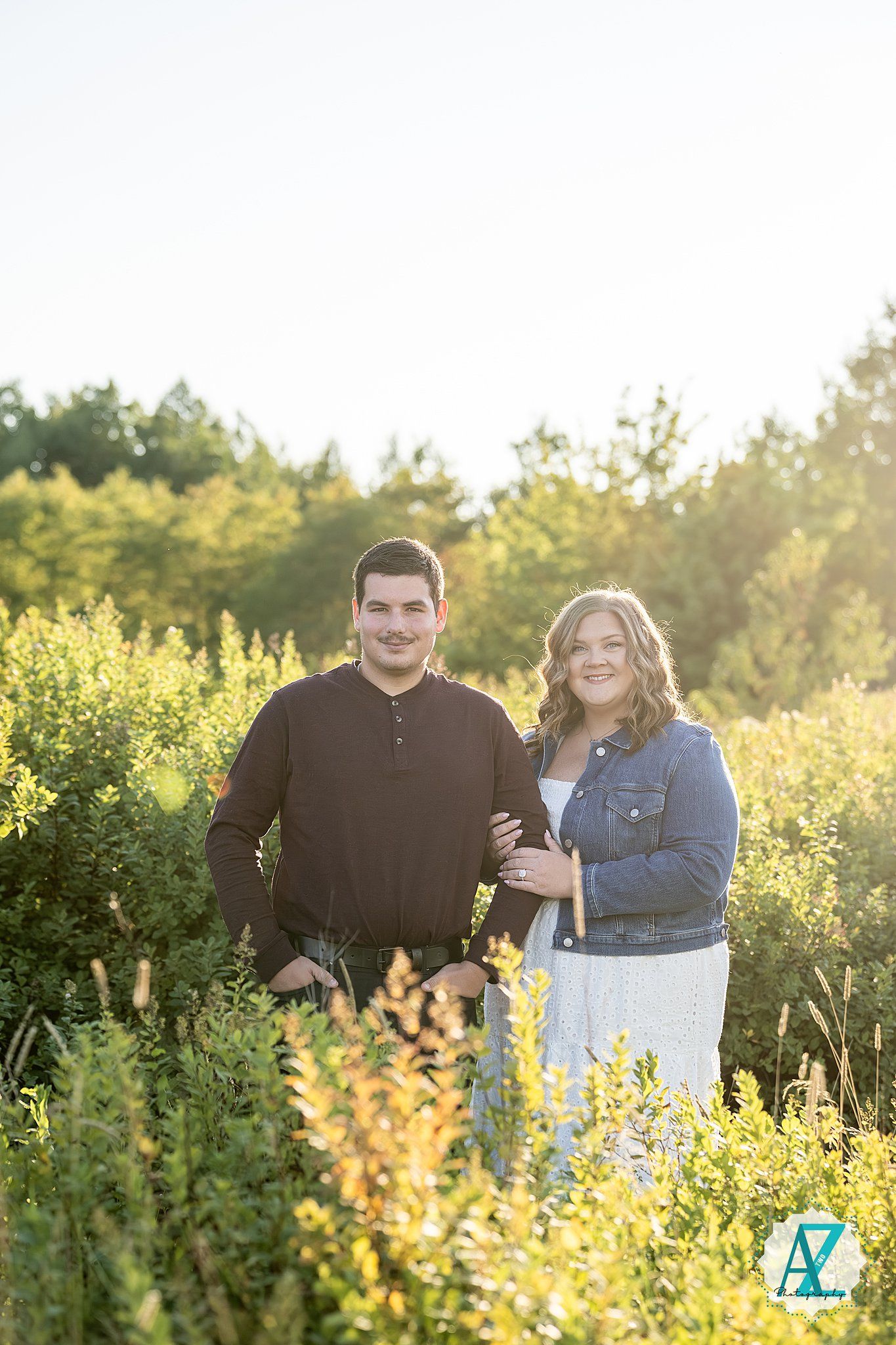 A romantic outdoor photoshoot showing a couple embracing in a golden sunlit meadow with wildflowers.
