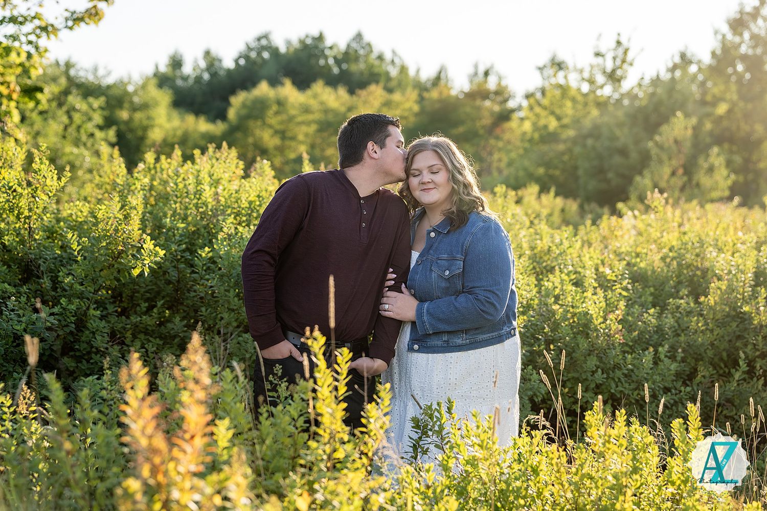 Romantic couple embraces in golden sunlit meadow of tall wildflowers during sunset photo session.