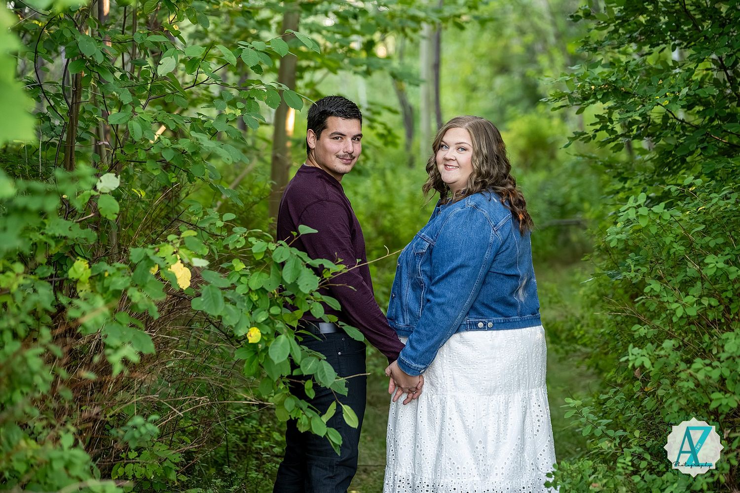 A couple embraces among green trees and foliage during an outdoor photography session.