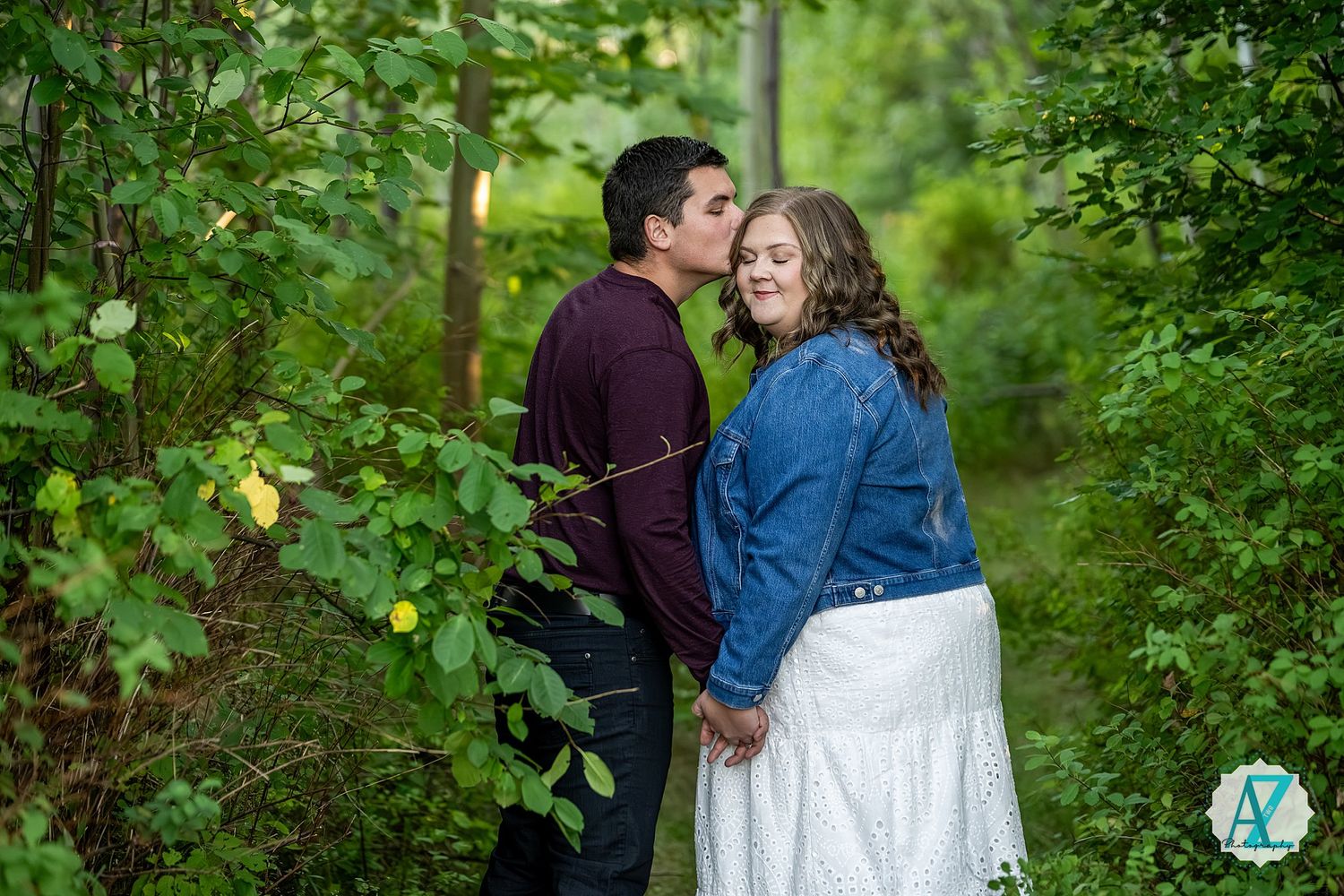 A couple shares a romantic moment together in a lush green forest setting during a photo session.
