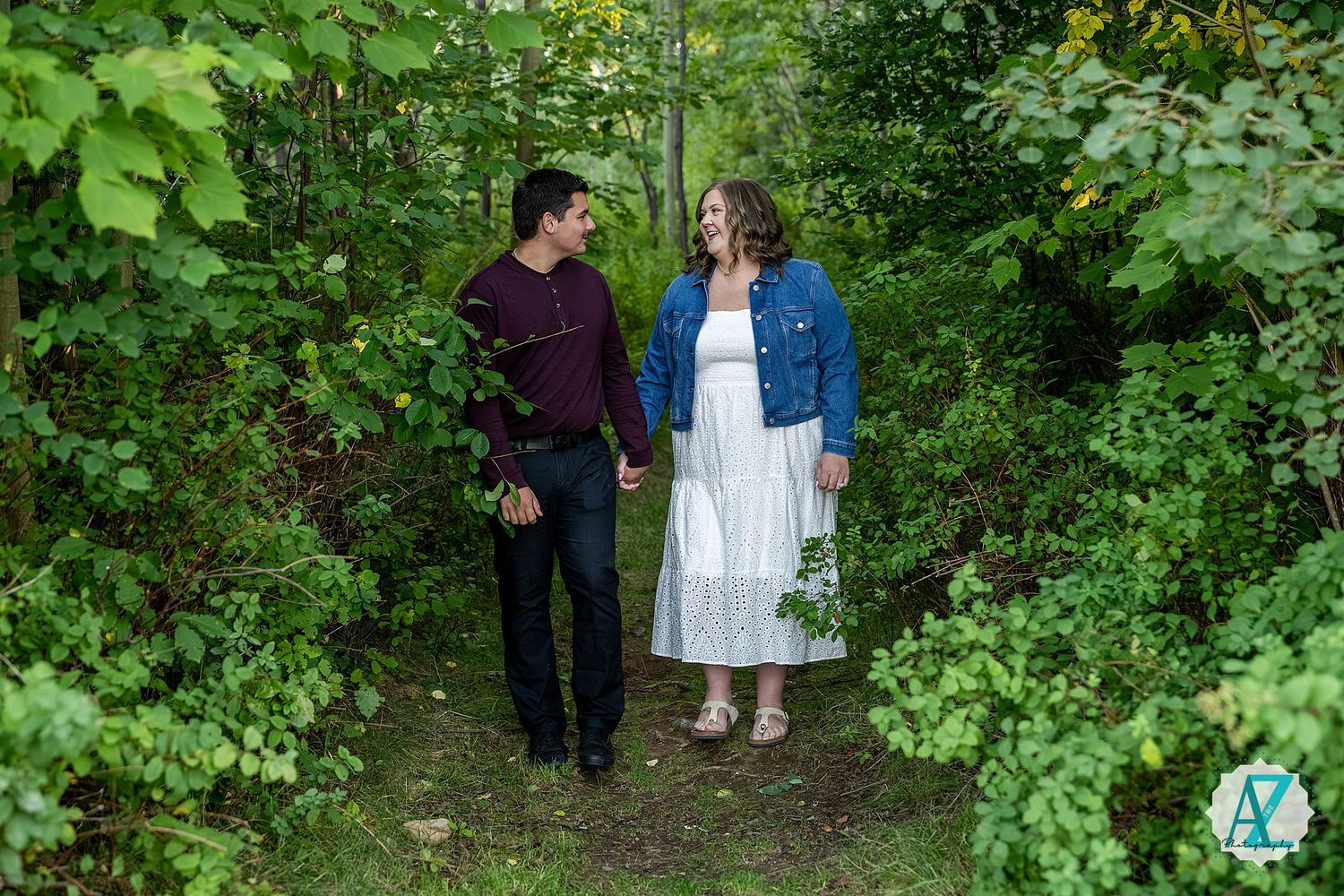 Two people stand amid lush greenery while wearing blue and white casual attire in an outdoor nature setting.