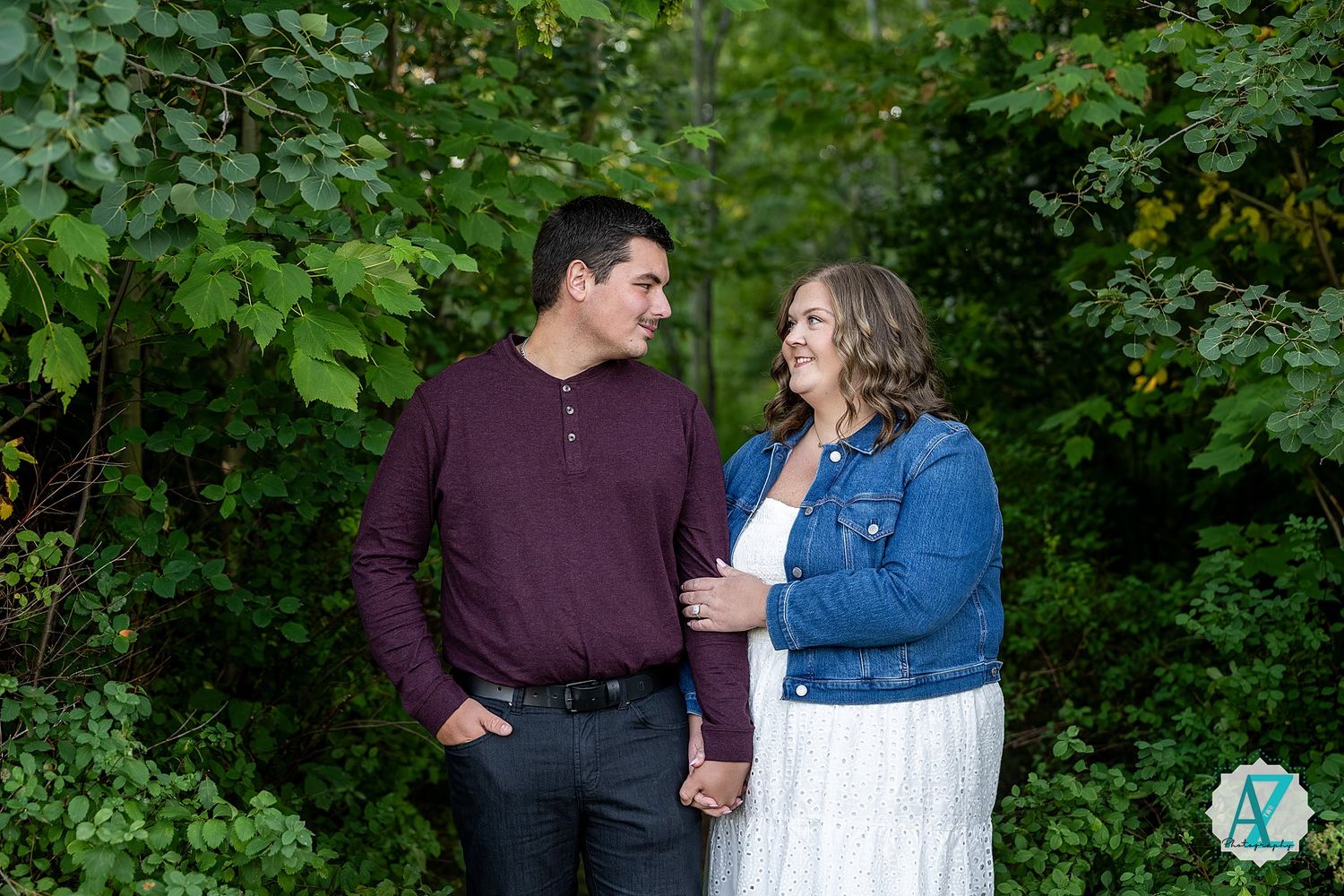 A romantic outdoor portrait of a couple sharing a tender moment among lush green trees.