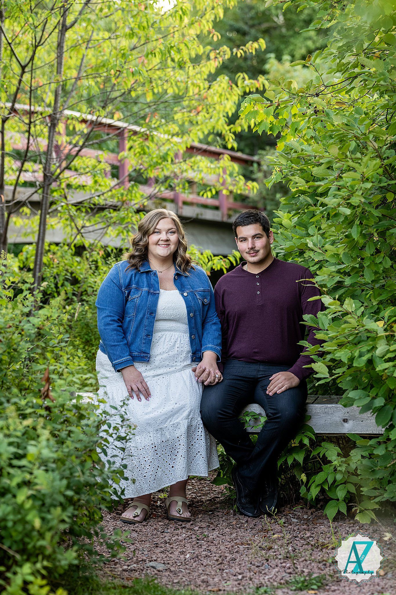 A couple relaxes together on a wooden bench in a garden setting with vibrant green foliage surrounding them.