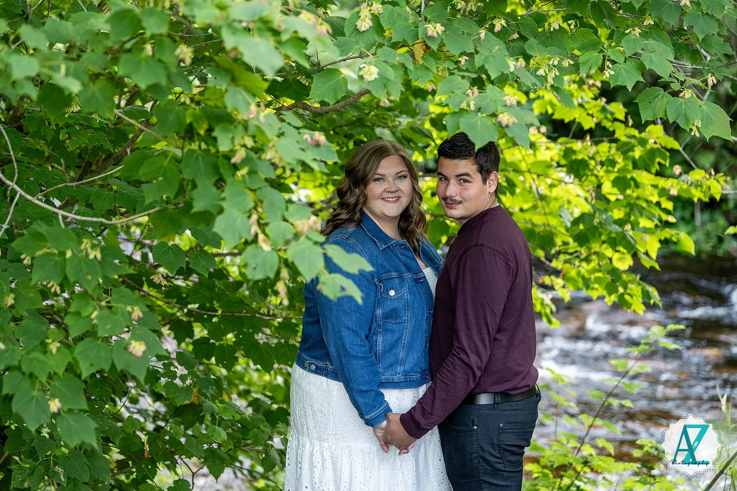 Couple sharing tender moments under lush green trees in an outdoor engagement photoshoot session.