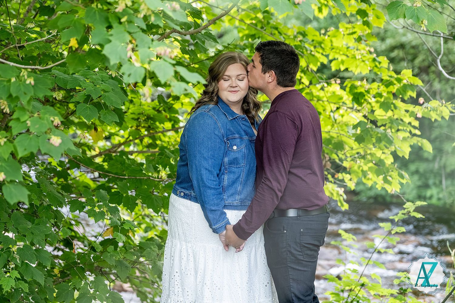 Couple sharing romantic moments in nature surrounded by vibrant green foliage on a sunny day.