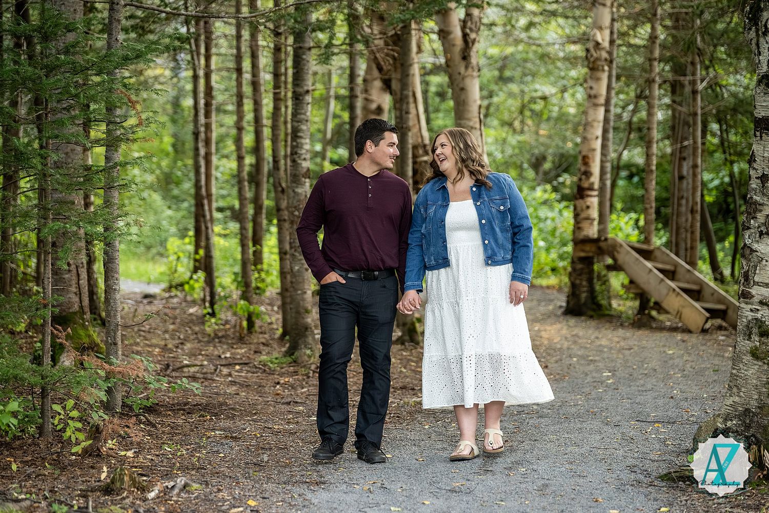 Two people walk hand in hand along a tranquil forest path surrounded by lush green trees and foliage.