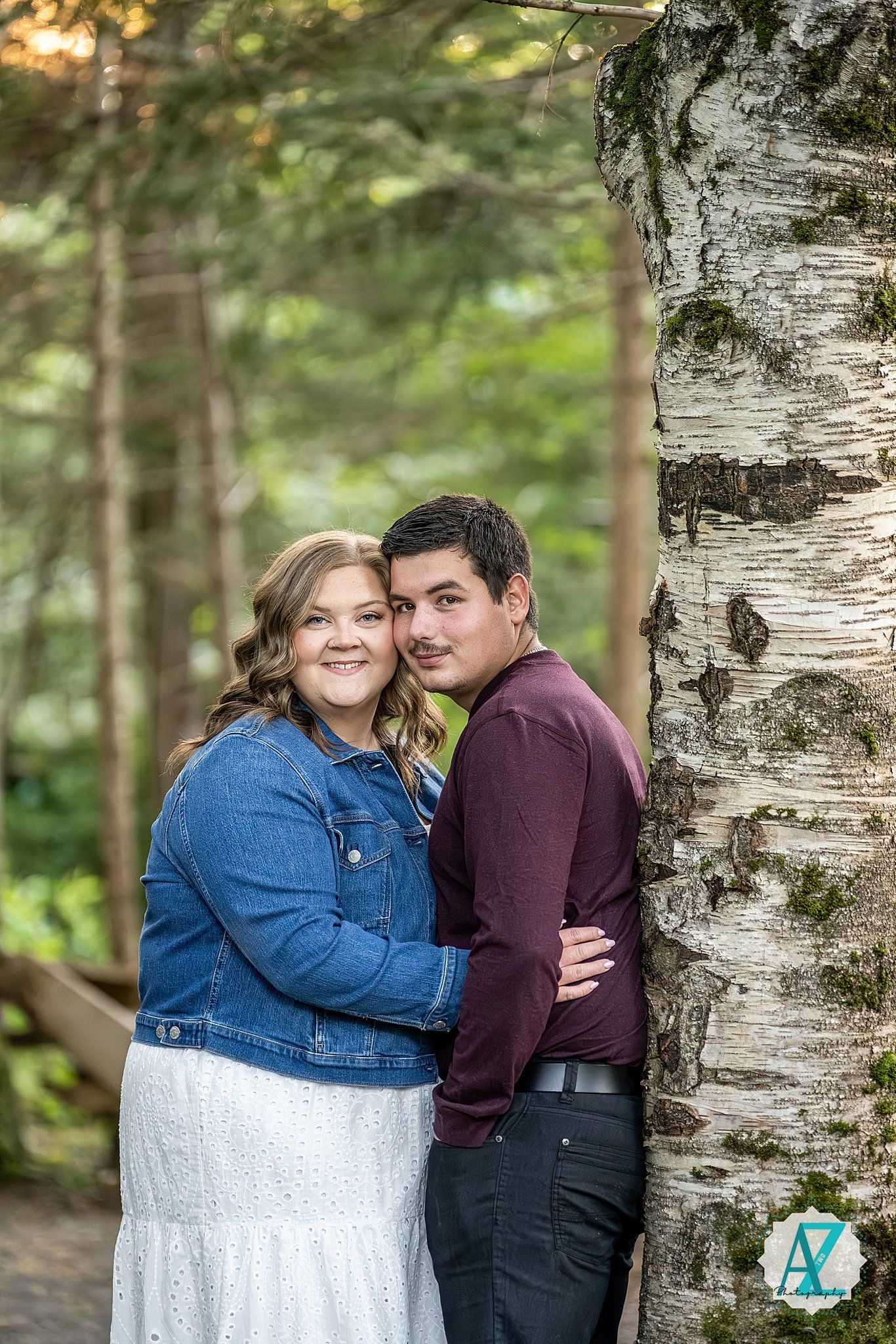 A romantic couple embraces near white birch trees in a dreamy forest setting with soft natural lighting.