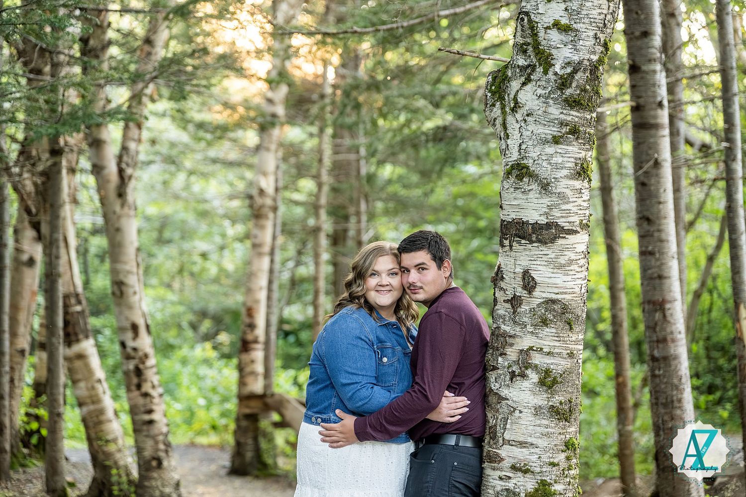 A couple shares an intimate moment among white birch trees in a lush forest setting during a photo session.