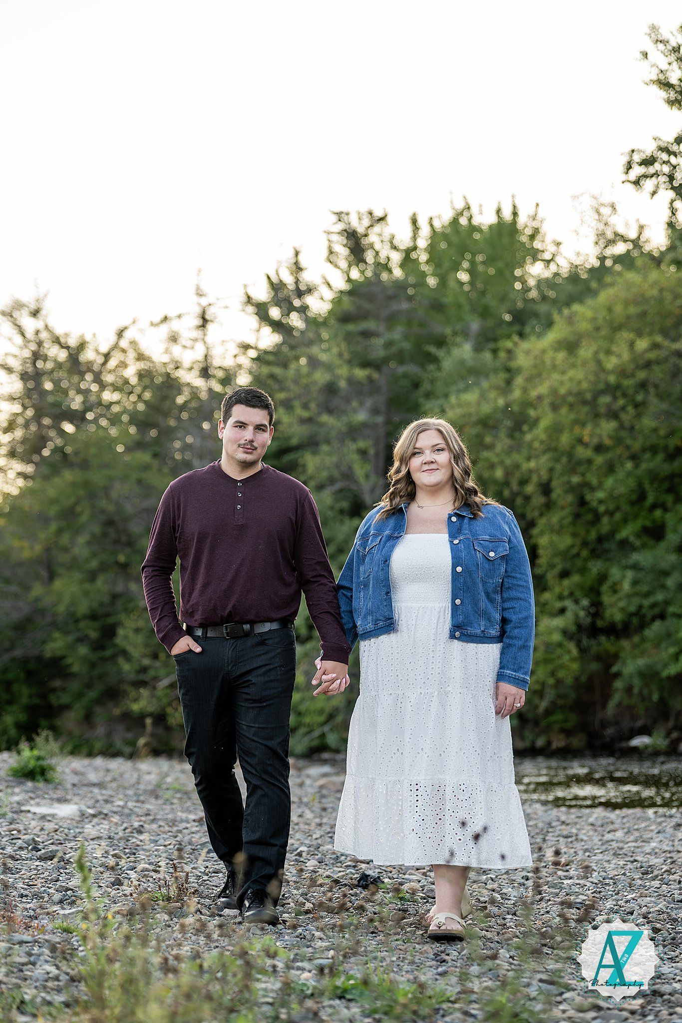 A couple walks together hand in hand along a rocky riverbank on a sunny autumn day.