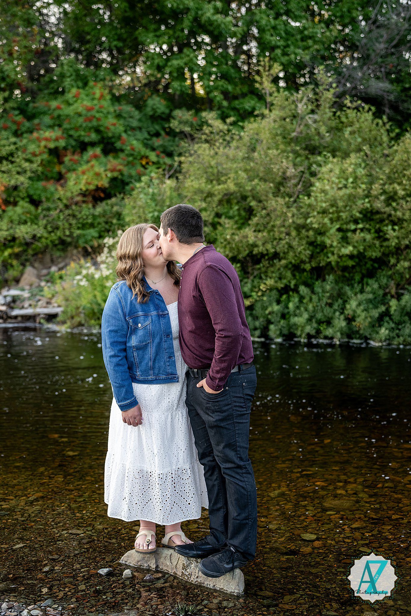 A romantic couple shares an intimate moment by a tranquil pond's edge surrounded by lush greenery.