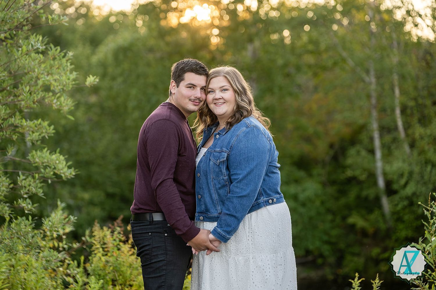 Couple sharing romantic moments at sunset in a lush green outdoor setting during their engagement photoshoot.
