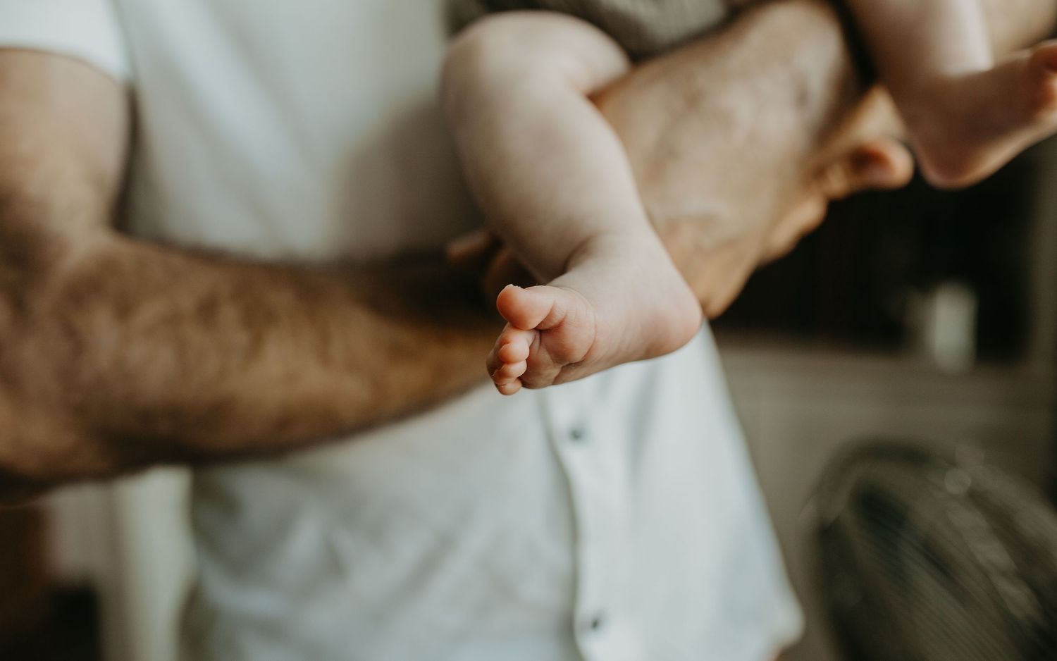 Close-up of a parent and baby's hands touching tenderly on white fabric in soft natural light.