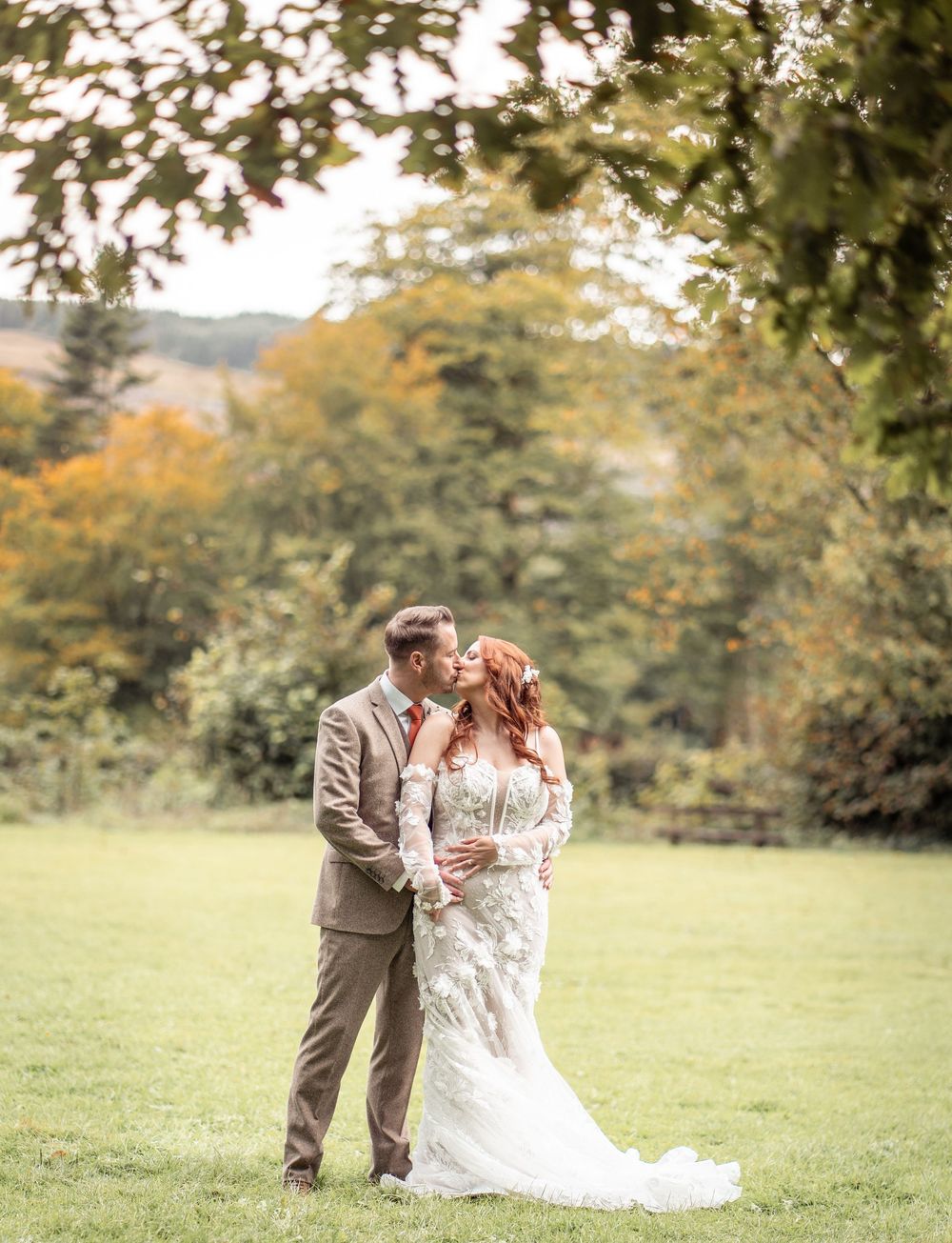 A couple shares an intimate moment in a lush autumn field wearing formal wedding attire.