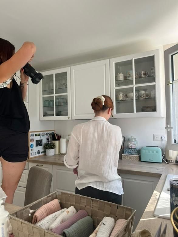Person cooking in modern white kitchen with glass cabinets while holding a serving spoon over stovetop.