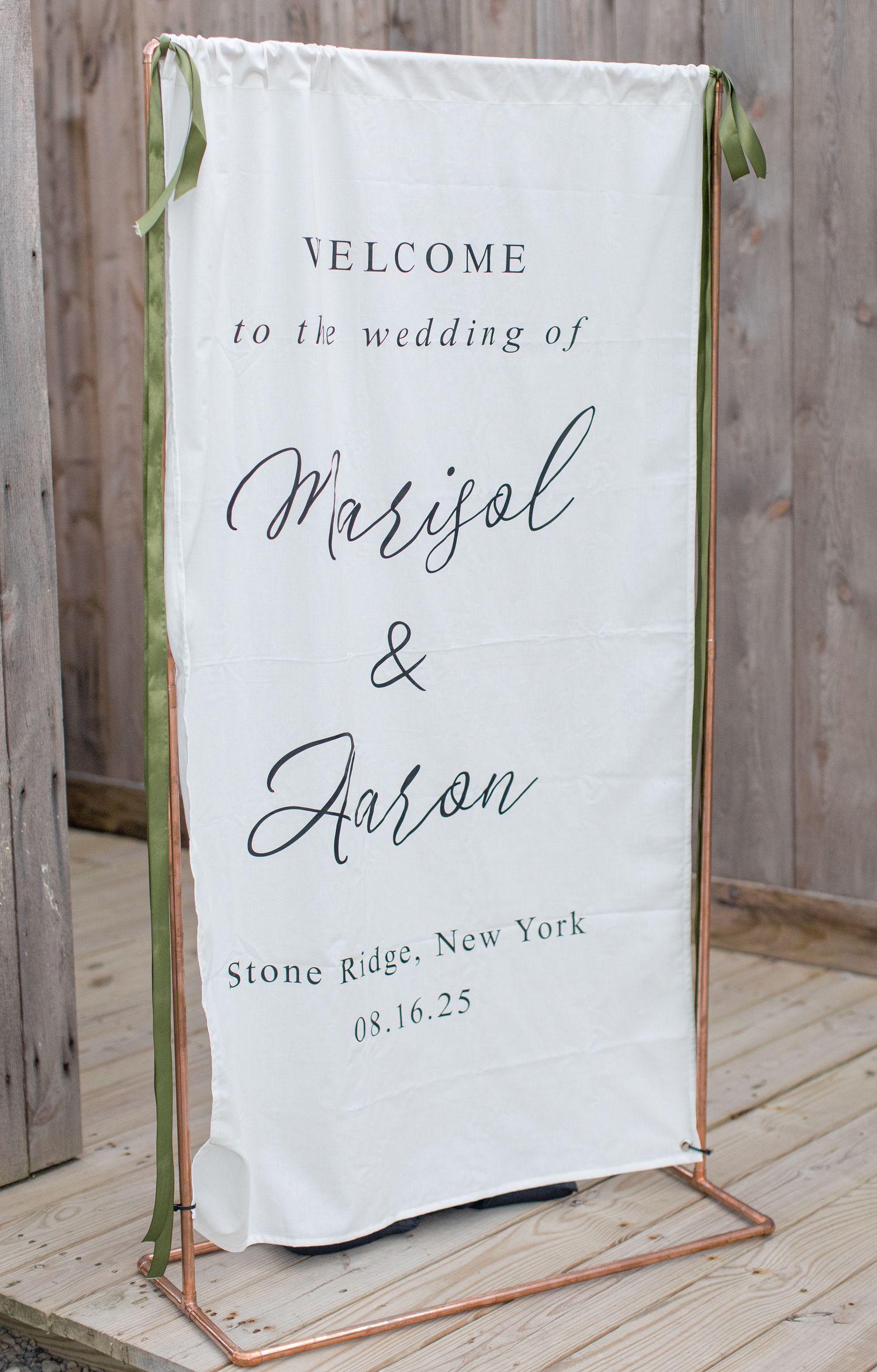 A white wedding welcome sign with elegant script font displaying names and Stone Ridge, New York location details.